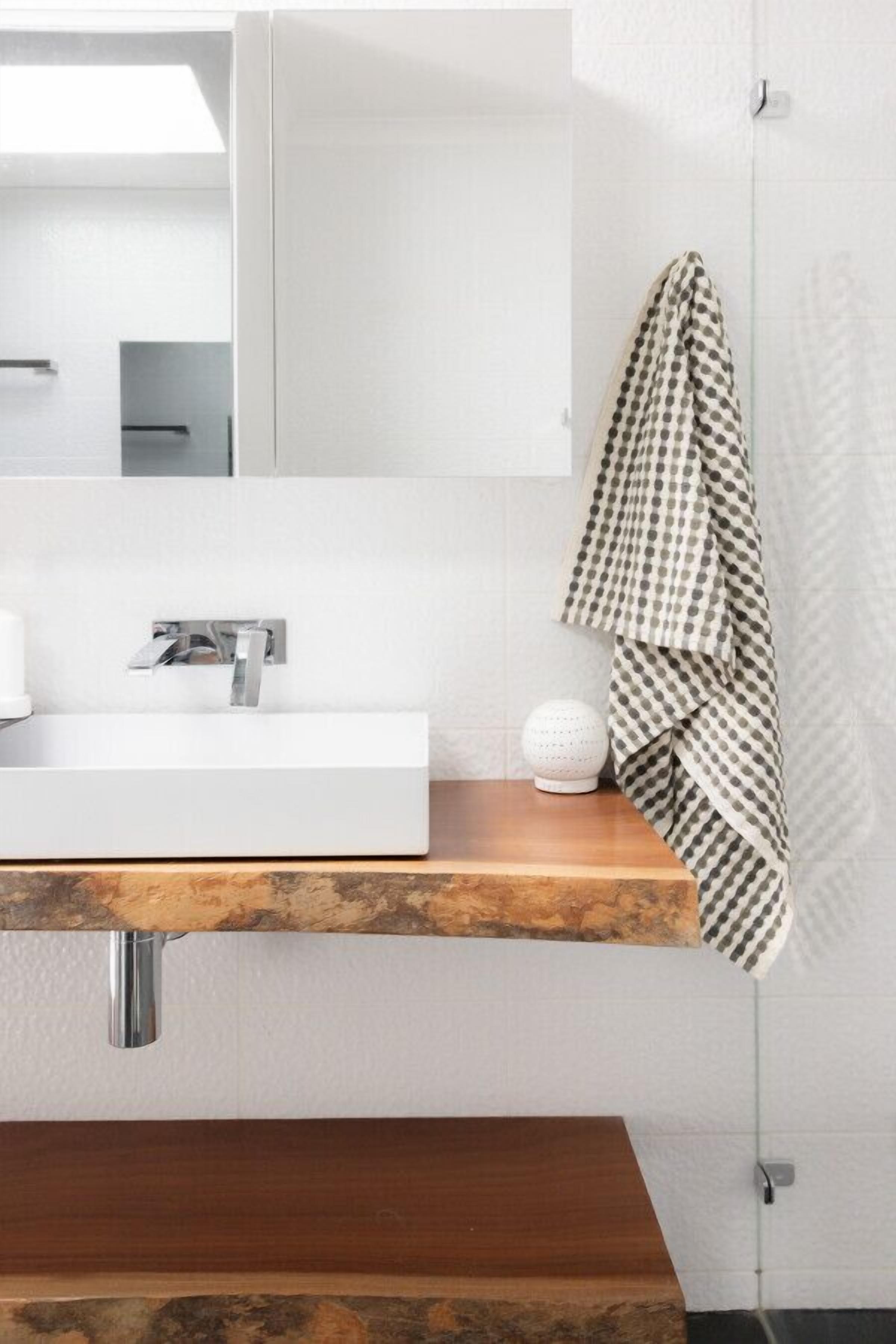 A modern bathroom with a wooden vanity, a white sink, a towel, and a spherical object on the counter.