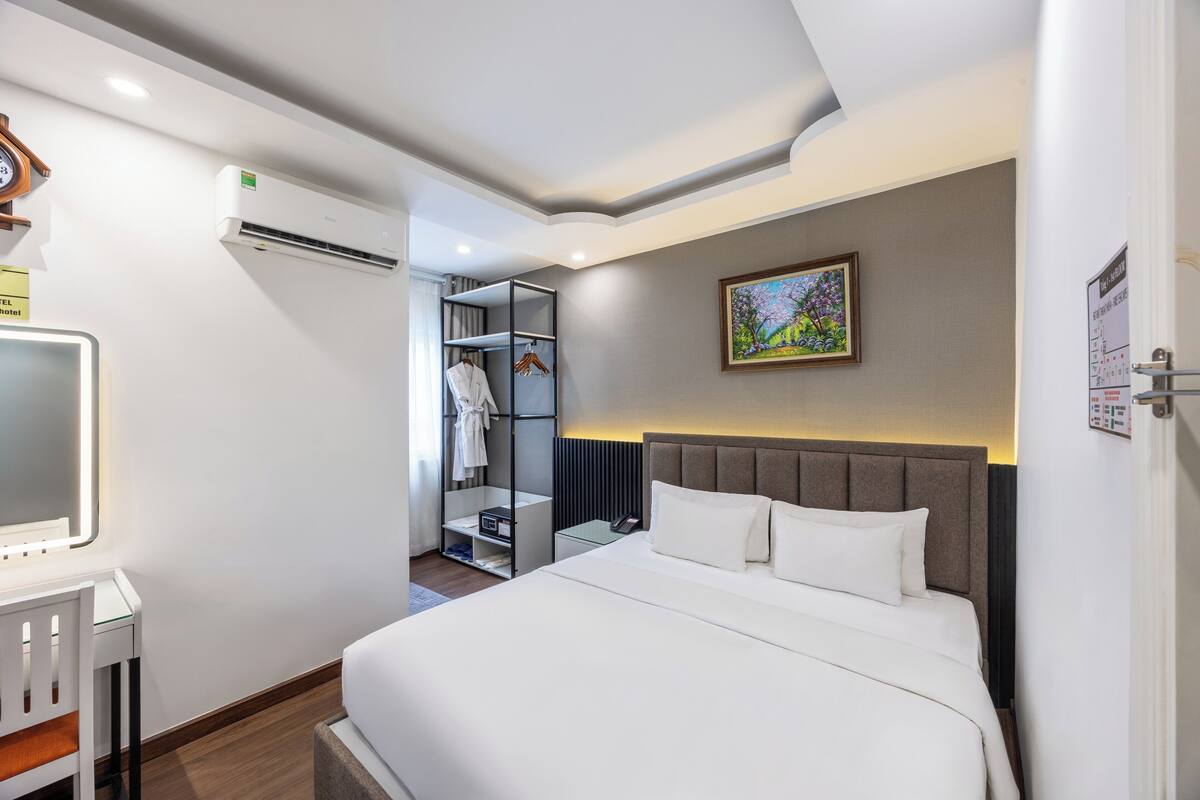 Ein Hotelzimmer mit einem Bett, einem Kleiderschrank, einem Schreibtisch mit Stuhl, einer Klimaanlage und einem Bild an der Wand.
