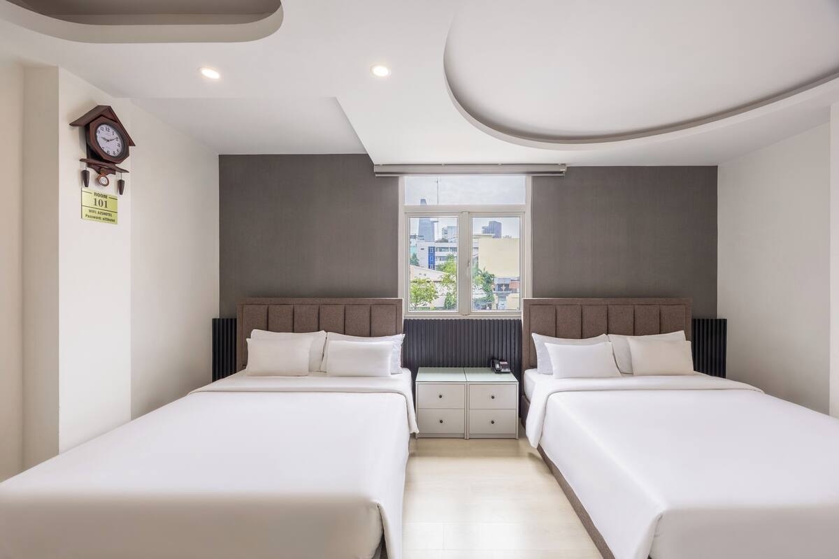 Ein Hotelzimmer mit zwei Betten, einer Wanduhr und einem Fenster mit Blick auf die Stadt.