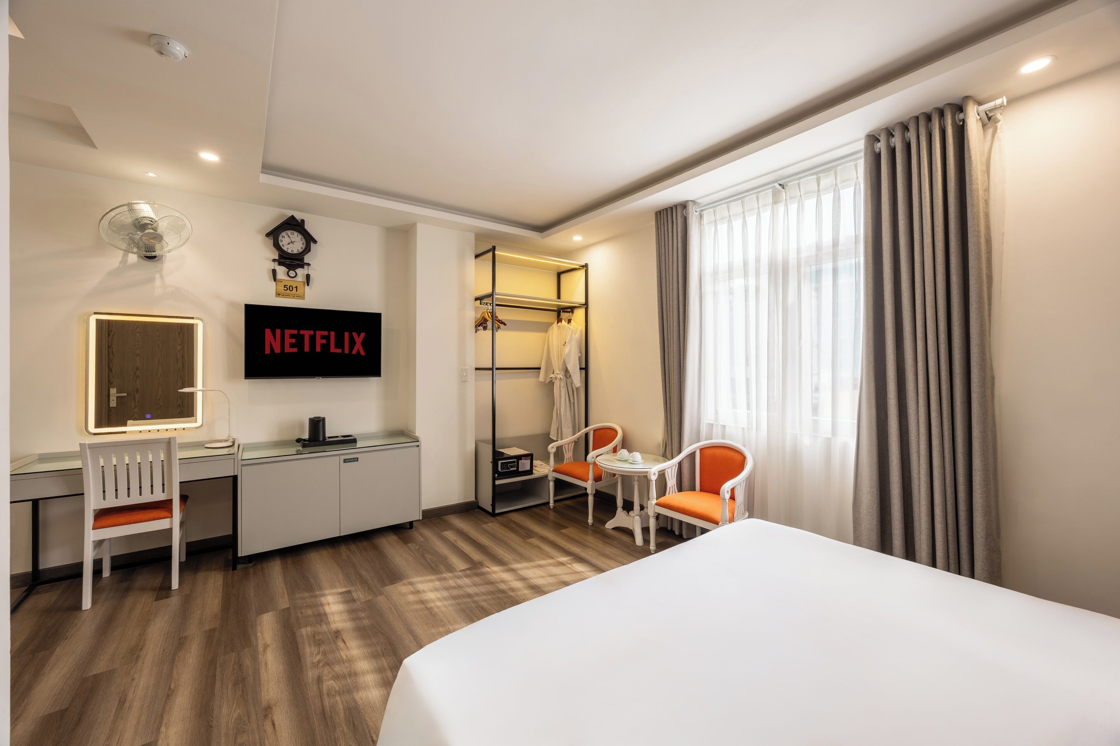 A hotel room with a bed, desk, chair, and a TV screen displaying "NETFLIX".