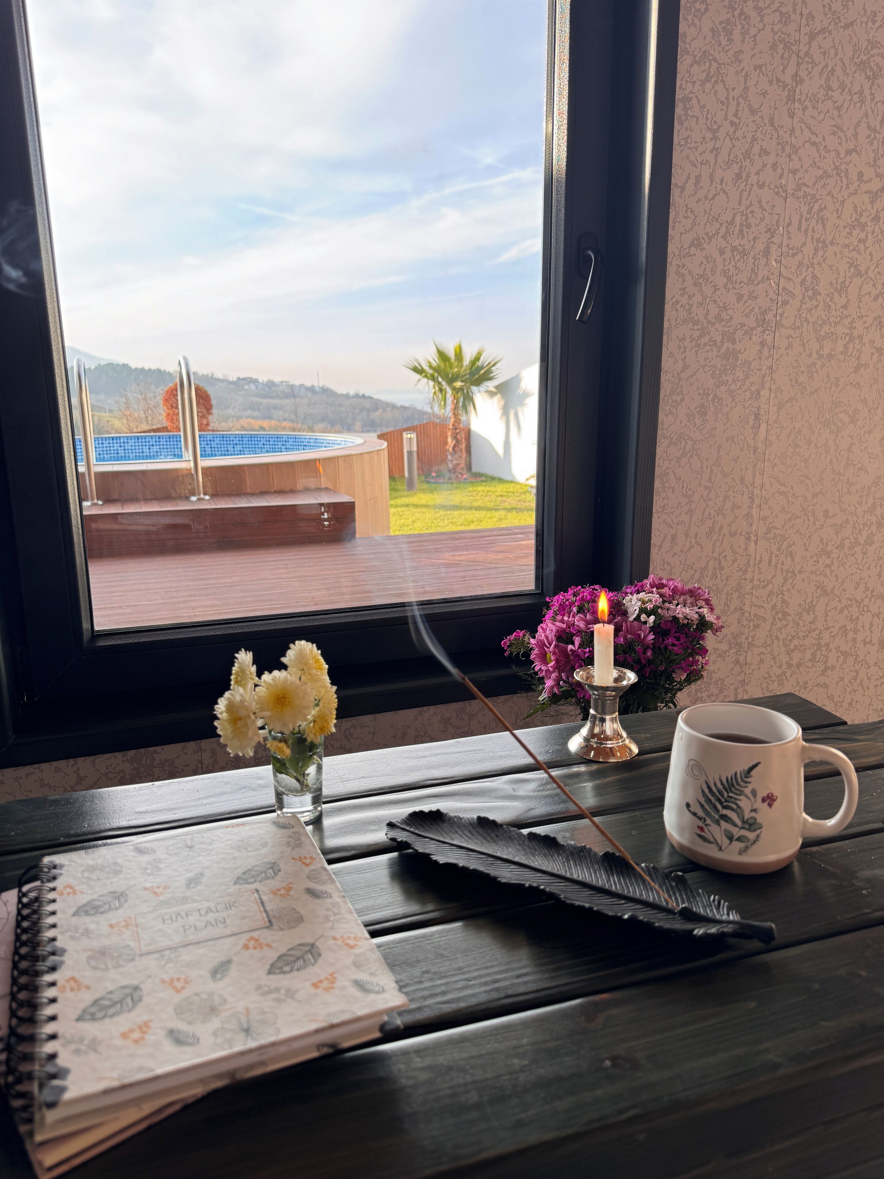 A wooden table with a notebook, a candle, and a mug.