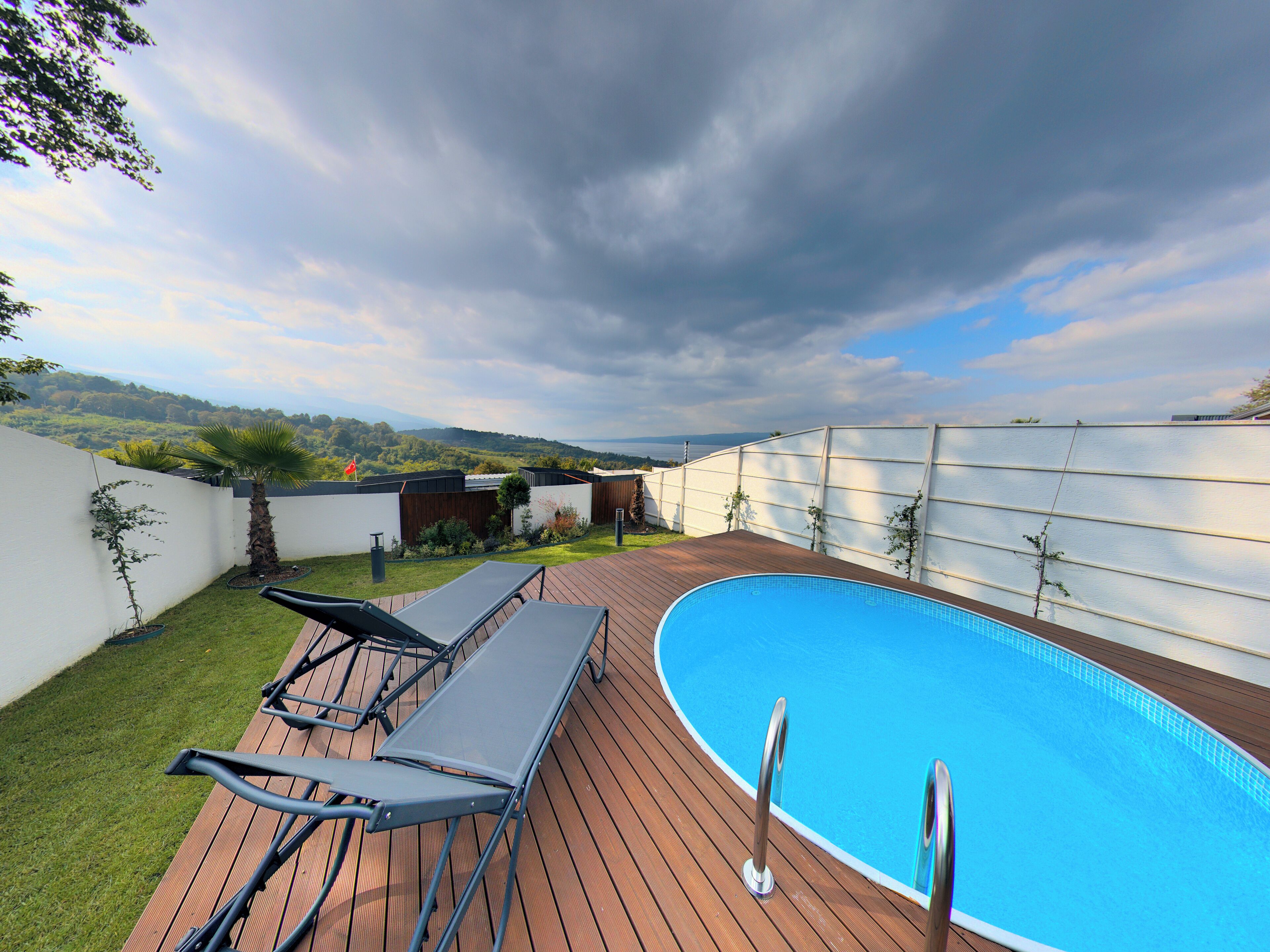 A swimming pool with a wooden deck, lounge chairs, and a view of the landscape.
