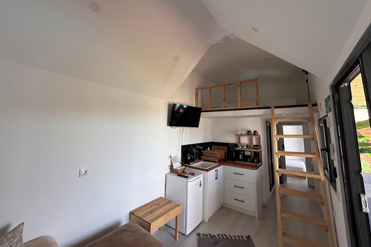 Una cocina compacta con televisión integrada, un refrigerador pequeño y una cama entrepiso de madera.
