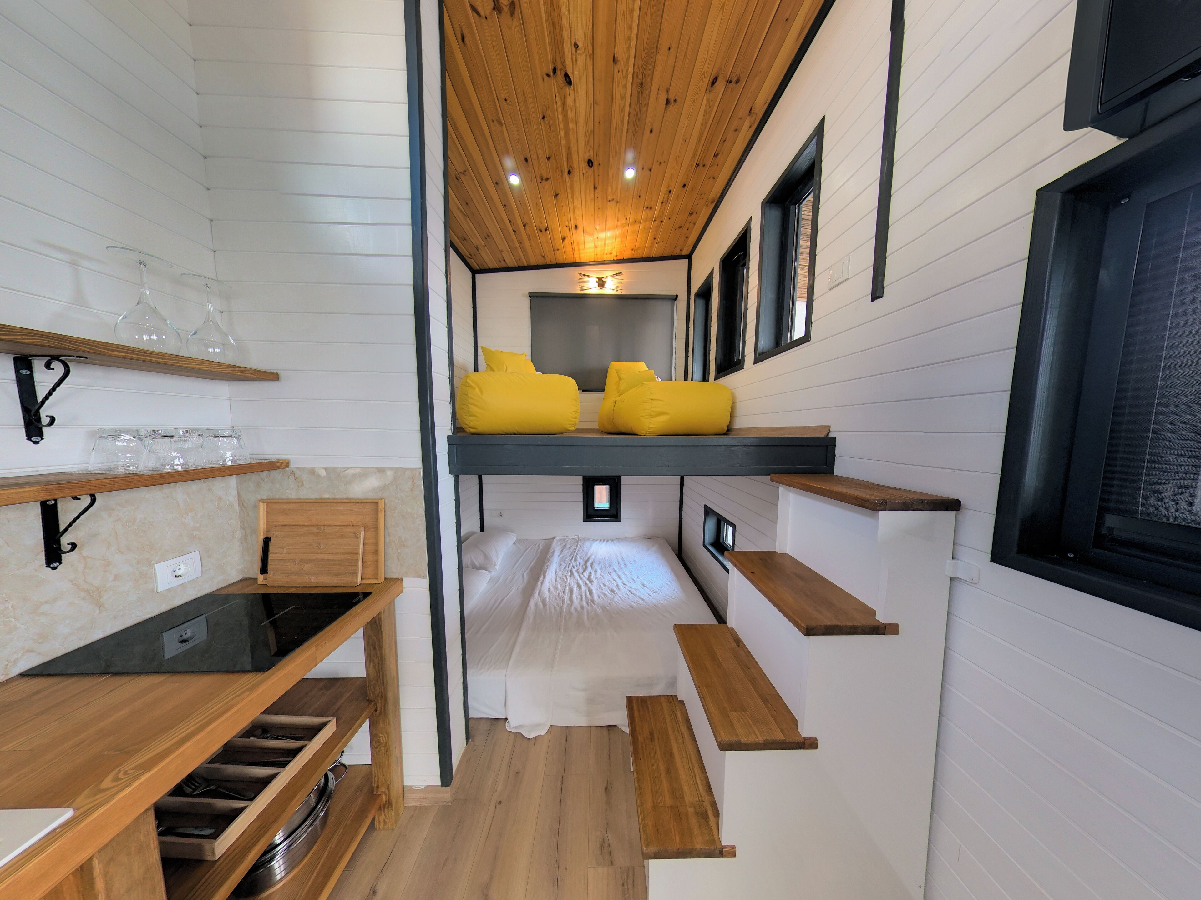 Un intérieur moderne et compact, doté d’un lit superposé, d’étagères en bois et d’un coin cuisine intégré.