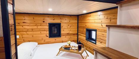 Una habitación compacta con estilo de cabaña, de madera, con literas, una mesita con provisiones para el desayuno y estantes empotrados.