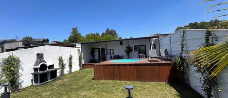 A backyard with a swimming pool, a barbecue area, and a wooden deck.