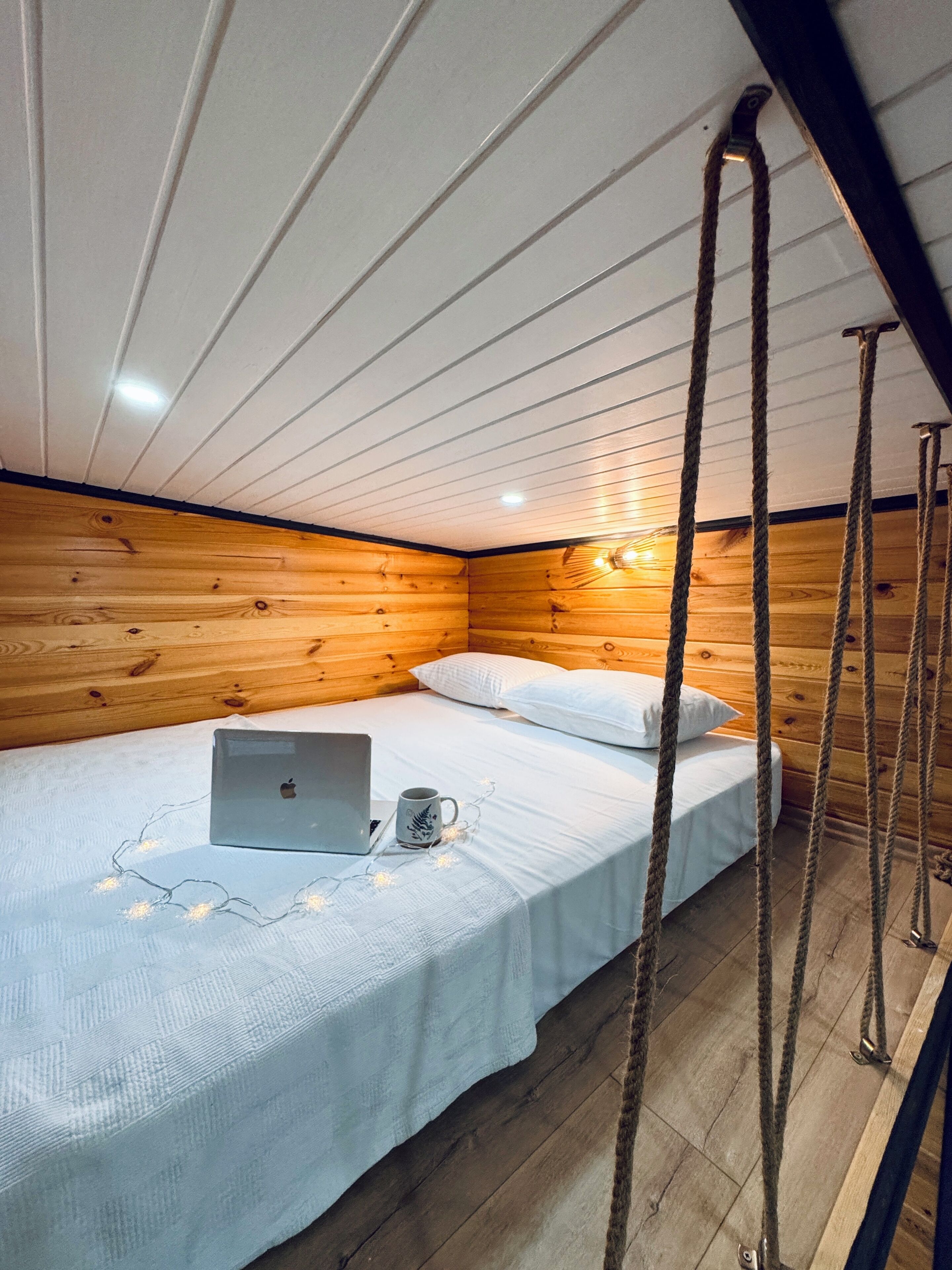 Een gezellig slaapkamer in een chalet met houten plafond, een bed met wit beddengoed, een laptop en een mok op het bed.