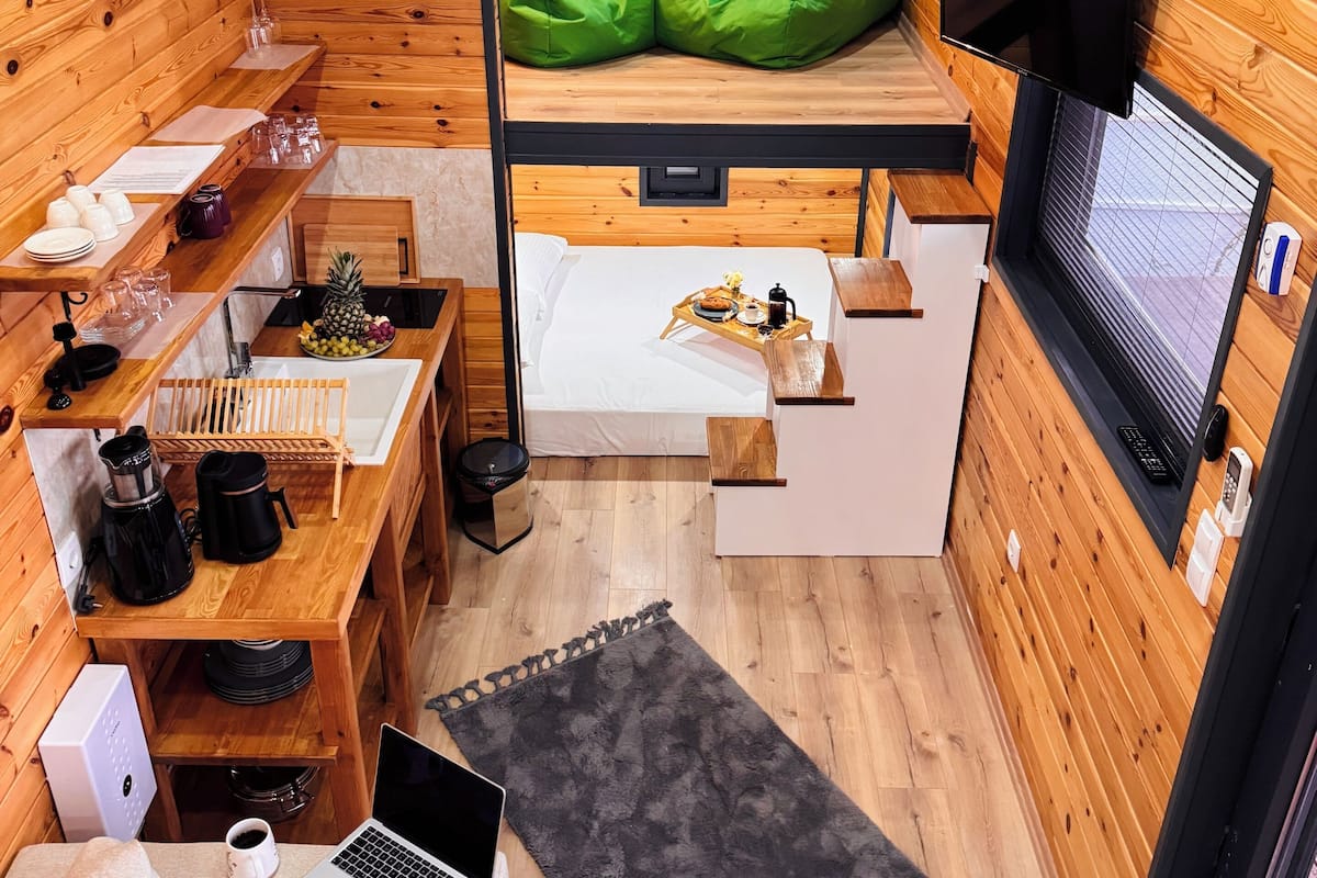 Una habitación compacta de estilo cabaña con literas, un escritorio con una computadora portátil, una cafetera y una pequeña zona de estar con un tapete.