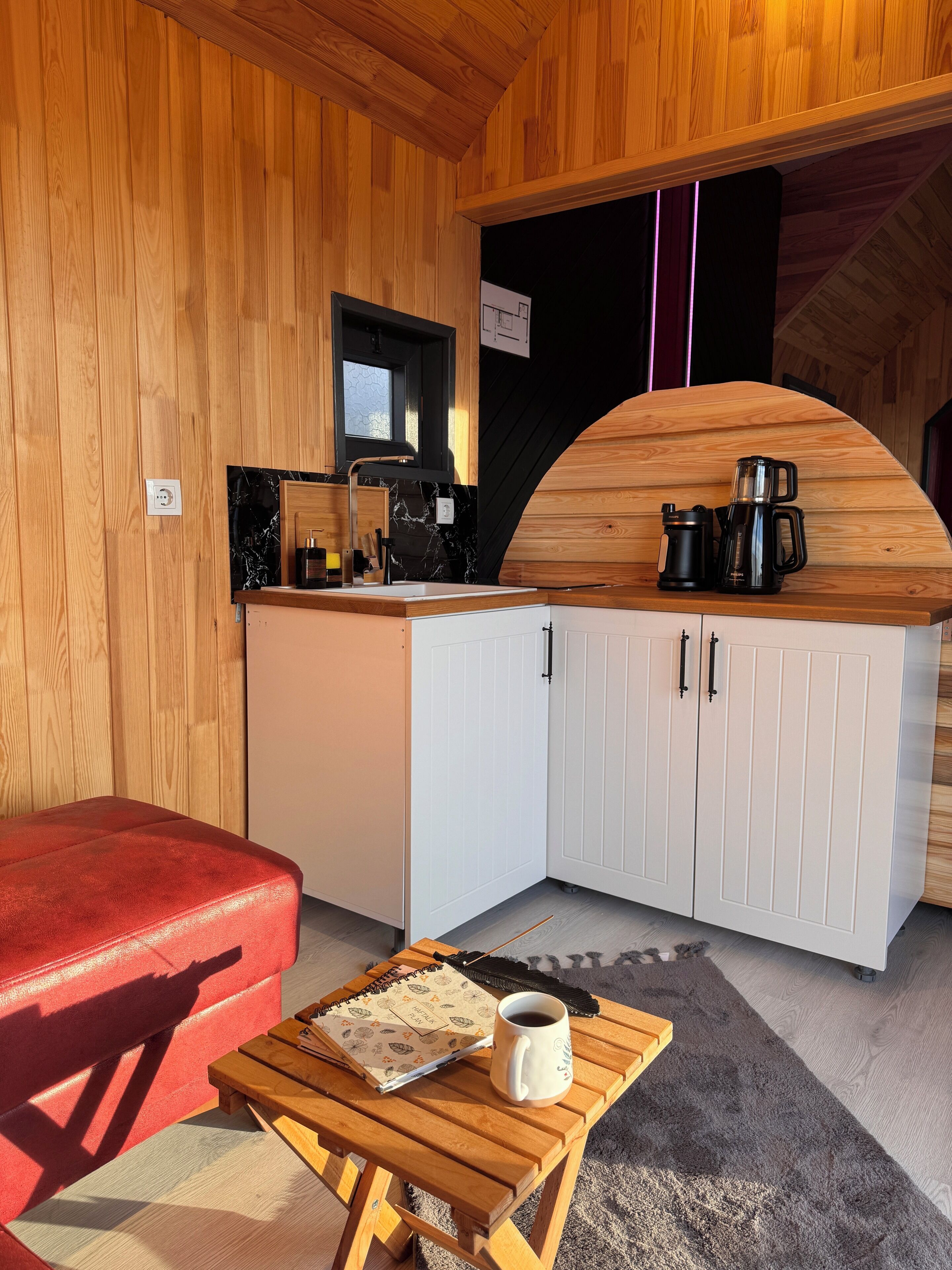 A compact kitchen with a wooden countertop, white cabinets, and a red couch.