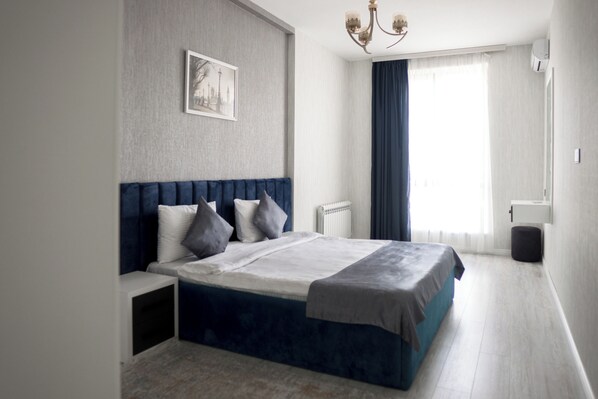 A modern bedroom with a large bed, a bedside table, a radiator, and a window with curtains.
