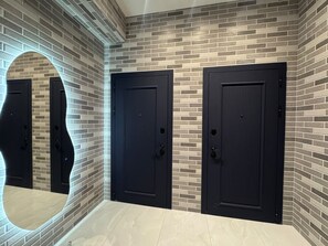 A hallway with a brick wall, three black doors, and a large mirror.