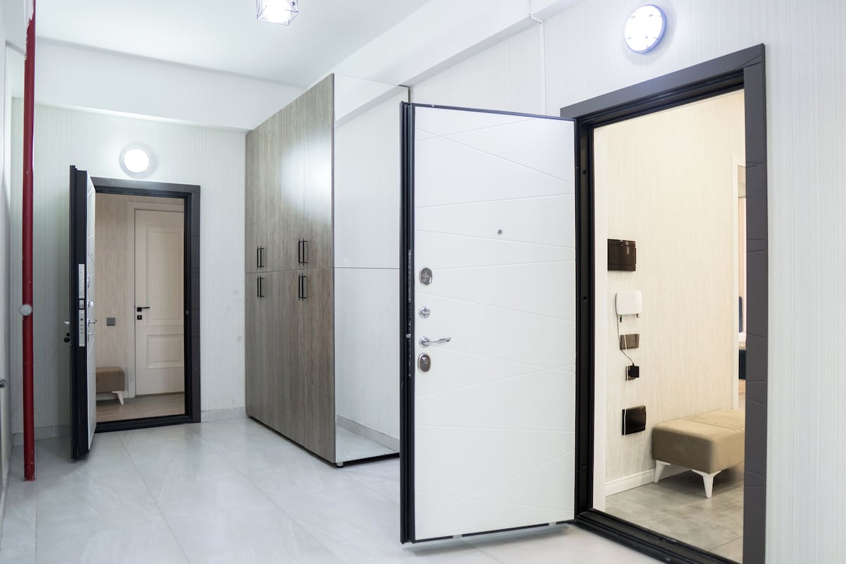 Un pasillo moderno de hotel con un armario de madera, una puerta blanca y un banco en una habitación.