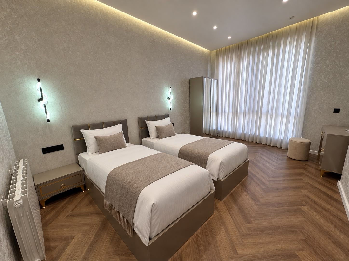 Una camera d'albergo moderna con due letti, una toeletta e un'ampia finestra con tende.
