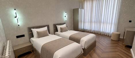 Una camera d'albergo moderna con due letti, una toeletta e un'ampia finestra con tende.