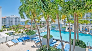 A rooftop pool area with palm trees, lounge chairs, and a view of the cityscape.
