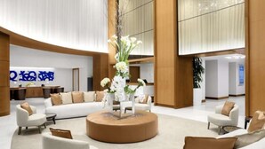 A spacious lobby with a central seating area, a reception desk, and a large mirror reflecting the space.