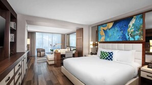 A hotel room with a large bed, a desk, a chair, a vanity, and a large painting on the wall.