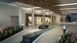 A modern hotel lobby with a car parked in the center, a fountain, and a unique ceiling design.