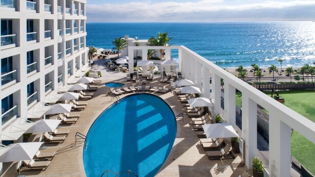 A hotel pool area with a view of the ocean, lounge chairs, umbrellas, and a large pool. - Luxury 1 /1.5 condo perfect for beach vacation (Fort Lauderdale)