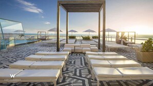 Eine Dachterrasse mit Liegestühlen und Sonnenschirmen mit Blick aufs Meer.