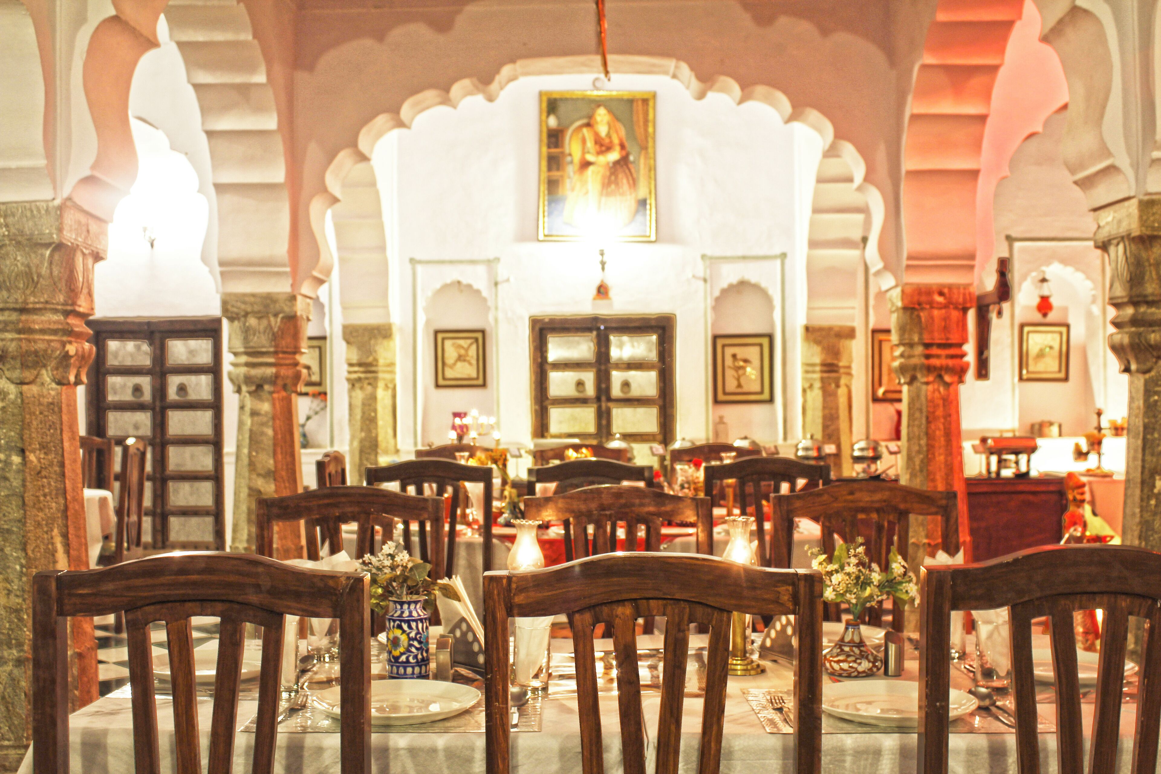 A dining area with wooden tables and chairs, a chandelier, and a painting on the wall.