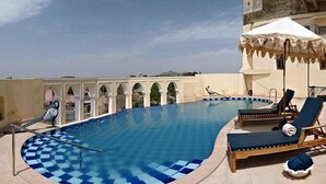 Una piscina en la azotea con bordes de azulejos azules, sillas de descanso y una marquesina blanca.