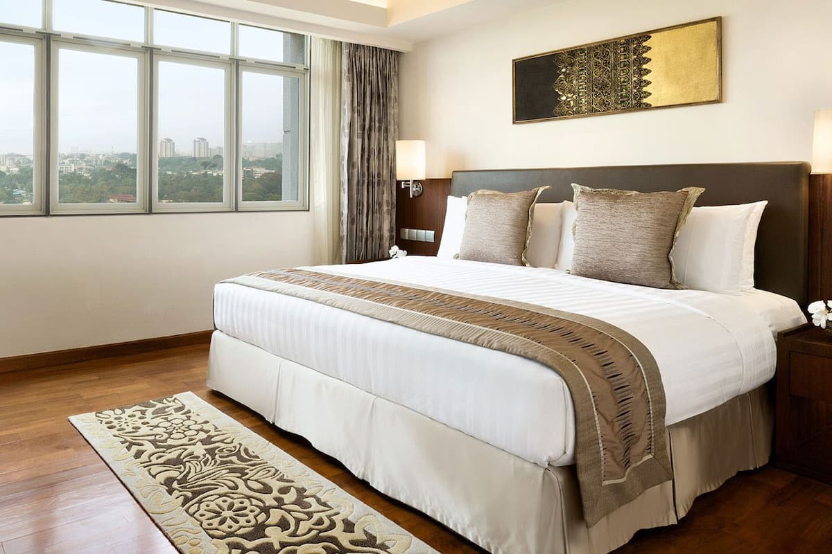 Ein Hotelzimmer mit einem großen Bett, einem Fernseher, einem Schreibtisch und Blick auf die Stadt durch große Fenster.