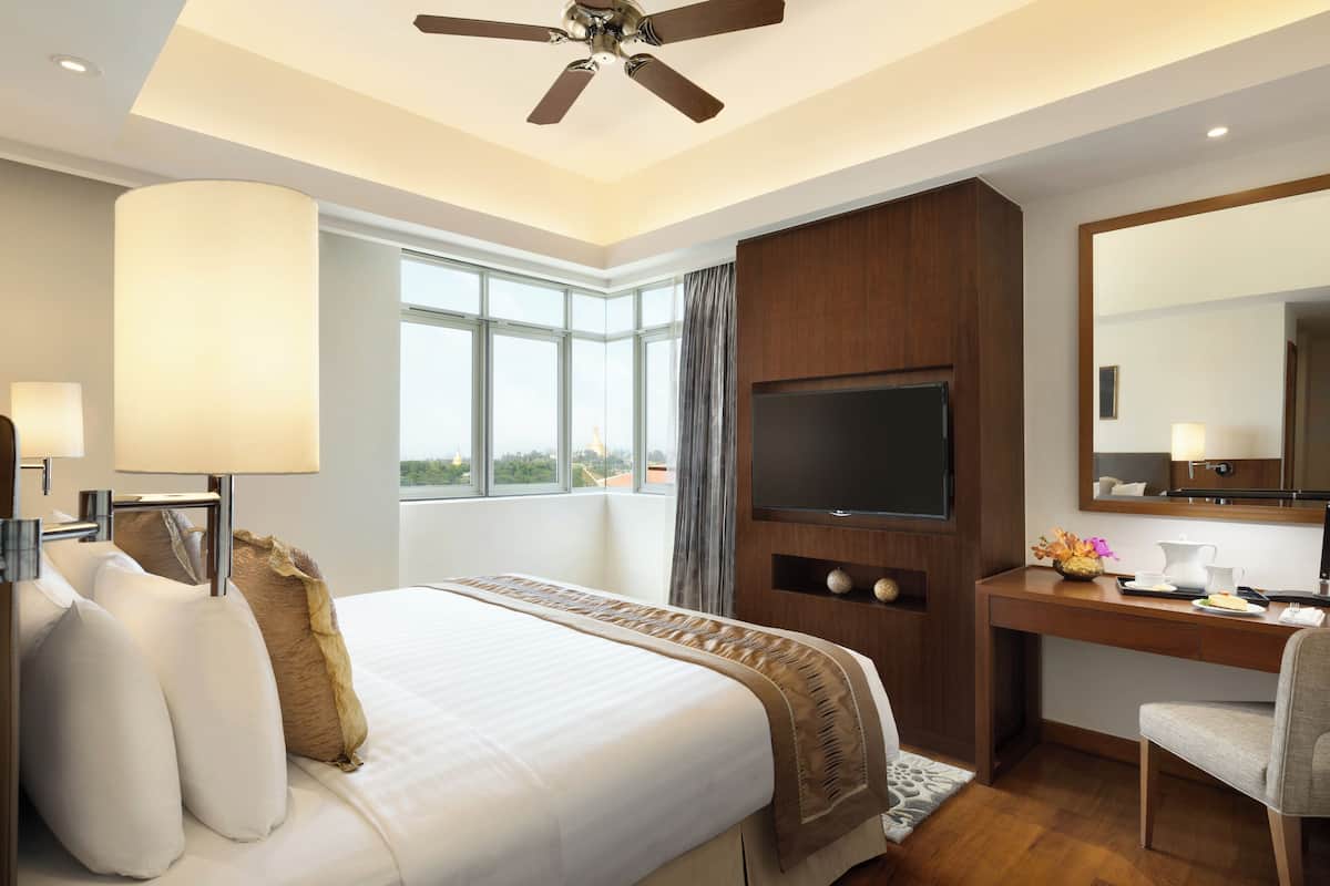 Ein Hotelzimmer mit einem großen Bett, einem Schreibtisch, einem Flachbildfernseher, einem Sessel und einem großen Fenster mit Blick ins Freie.