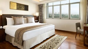 A hotel room with a large bed, a desk with a chair, a television, and a view of the city through large windows. - Shangri-La Serviced Apartments, Yangon (Yangon)