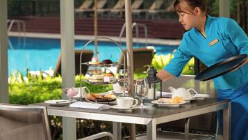 Mesa lista para un servicio de té, con vista a una piscina al fondo.