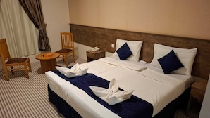 A hotel room with a large bed, a wooden chair, a small table, and a nightstand with a phone. - Retaj Alhayat (Makkah)