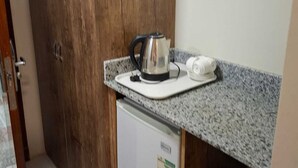 A compact kitchen with a wooden door, a small refrigerator, and a countertop with a kettle and a white appliance. - Retaj Alhayat (Makkah)