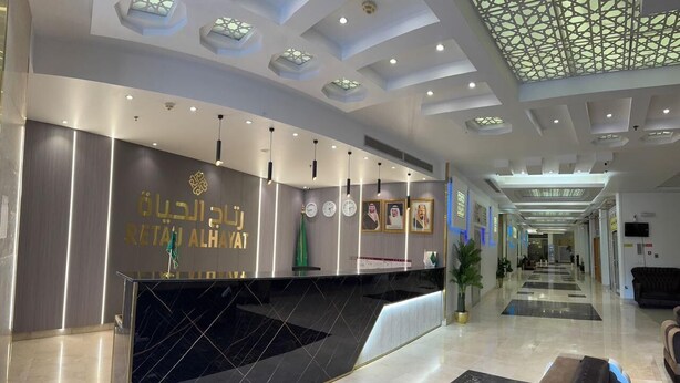 A modern hotel lobby with a reception desk, a geometric ceiling design, and a long corridor with seating areas. - Retaj Alhayat (Makkah)