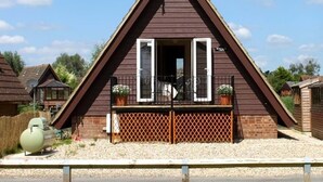 A triangular-roofed building with a balcony, a satellite dish, and a small garden area. - River Lark Lodge (Isleham)
