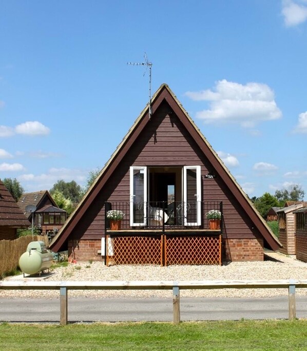 A triangular-roofed building with a balcony, a satellite dish, and a small garden area. - River Lark Lodge (Isleham)