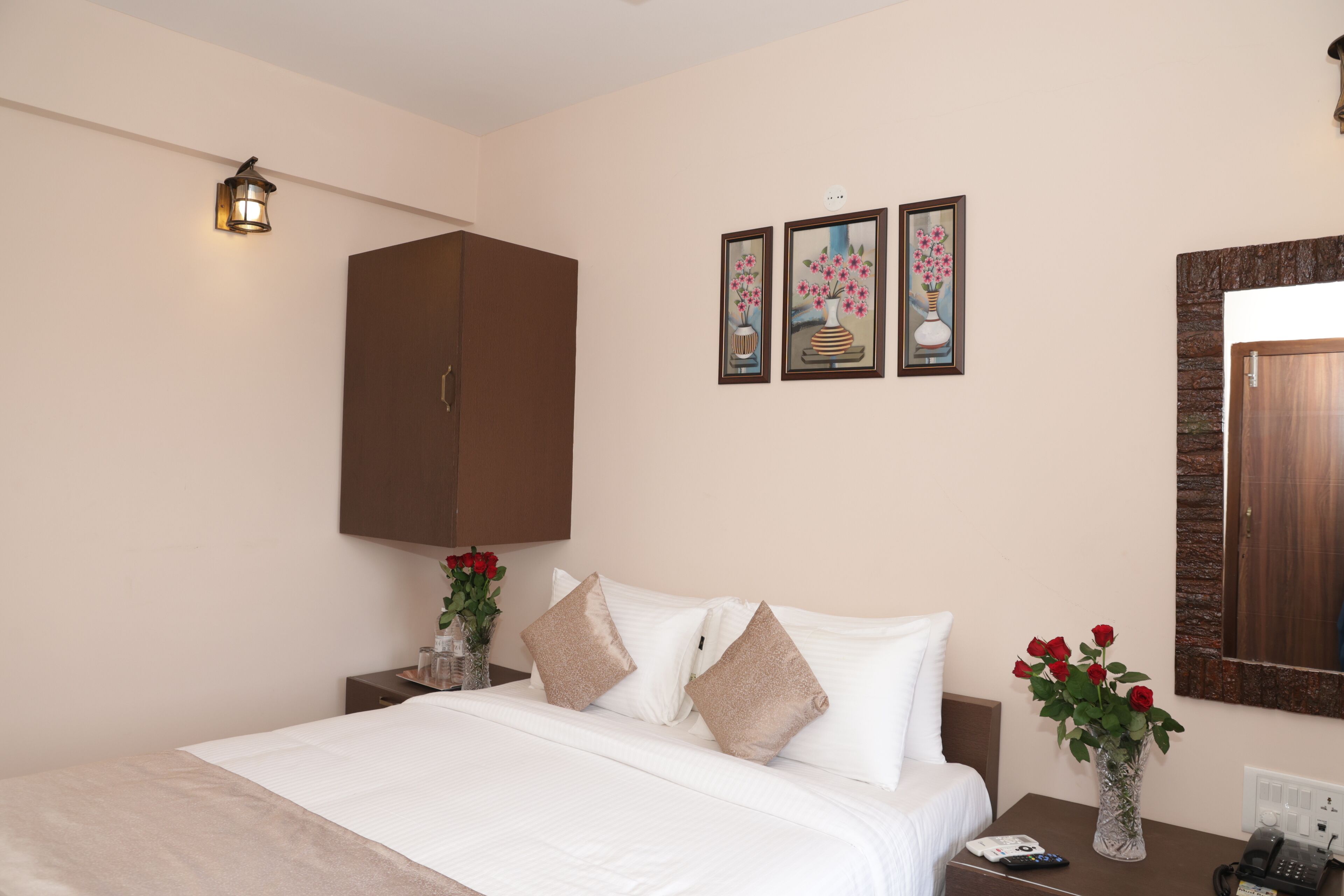 A hotel room with a bed, a nightstand, a vase with flowers, and a wall-mounted light fixture.