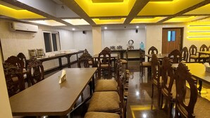 A dining area with wooden tables and chairs, a long counter, and a ceiling with yellow lighting. - Nazri Hotel (Arambol)