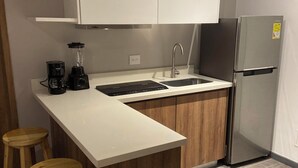A modern kitchen with white cabinets, a stainless steel refrigerator, a built-in island with stools, and a coffee maker. - Charming 1-bedroom apartment in Barranquilla (Barranquilla)