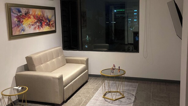 A modern living room with a beige sofa, a glass coffee table, and a painting on the wall. - Charming 1-bedroom apartment in Barranquilla (Barranquilla)