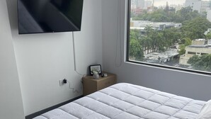 A modern hotel room with a large bed, a television mounted on the wall, and a window offering a city view. - Charming 1-bedroom apartment in Barranquilla (Barranquilla)