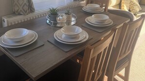 A dining area with a table set for four, a radiator, and a window with curtains. - 2-bed Cabin, Sleeps 4 in Cayton Bay (Scarborough)