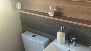 A compact bathroom with a toilet, sink, and a small shelf with a bird decoration. - 2-bed Cabin, Sleeps 4 in Cayton Bay (Scarborough)