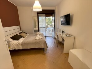 Un dormitorio moderno con cama, escritorio, televisor y balcón con mobiliario exterior.