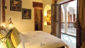 A hotel room with a bed, framed pictures on the wall, a balcony with a view, and a traditional lamp. - Luxurious Authentic Riad in the heart of the Medina (Morocco)