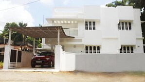 A modern two-story building with a covered carport, a red car parked inside, and a white exterior.