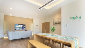 A modern living room with a grey sofa, wooden flooring, a TV on the wall, and a dining area with a table and benches.