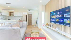 A modern living room with a flat-screen TV, a sofa, and a kitchen in the background.