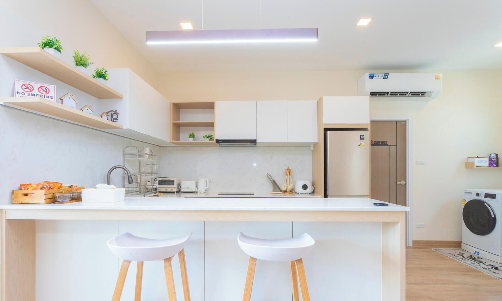 A modern kitchen with white cabinets, a central island with stools, a built-in oven, and a washing machine.