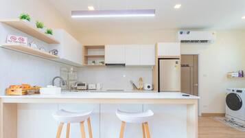 A modern kitchen with white cabinets, a central island with stools, a built-in oven, and a washing machine.