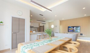 A modern living room with a dining area, a kitchen in the background, and a TV mounted on the wall.